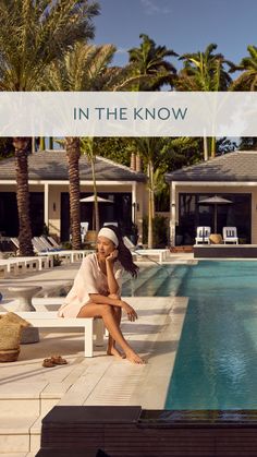 a woman sitting on the edge of a swimming pool with palm trees in the background