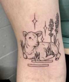 a small tattoo of a sheep laying down on the ground with flowers in the background