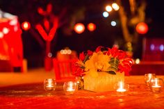 a table with candles and flowers on it in front of some red lanterns at night