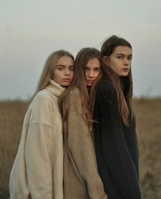 three women standing next to each other in a field