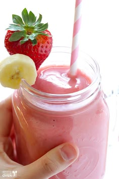 a hand holding a strawberry and banana smoothie in a mason jar with a straw