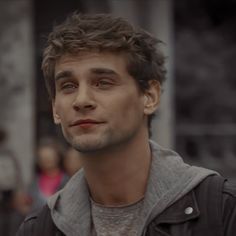 a young man standing in front of a building while wearing a jacket and looking at the camera