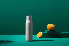 two oranges sitting next to a white bottle on a green surface with one cut in half