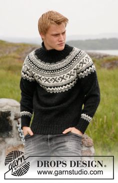 a young man wearing a black and white sweater standing in front of a stone wall