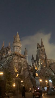 the hogwarts castle is lit up at night with people walking in front of it