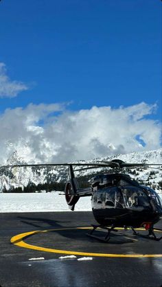 a helicopter sitting on top of an airport tarmac next to snow covered mountains in the background