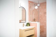 a bathroom with a sink, mirror and shower stall in the corner that has pink wallpaper on it