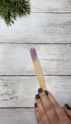 a woman's hand holding a wooden spatula with green nail polish on it