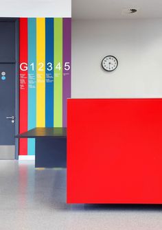 a brightly colored reception counter in an office building with a clock mounted on the wall