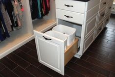 an open drawer in a closet with clothes hanging on the wall and other items behind it