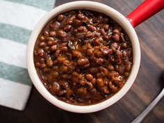 a white bowl filled with beans sitting on top of a table next to a red spoon