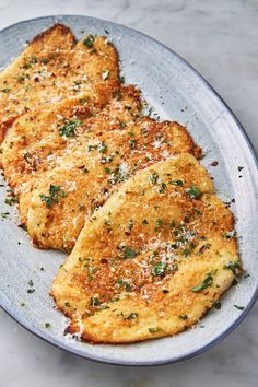 two pieces of fried chicken on a plate with parmesan cheese and herbs sprinkled on top