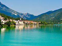 the water is very blue and green with houses on it's sides in front of mountains