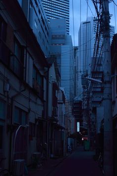 an alley way with tall buildings in the background at night, and one person walking down it