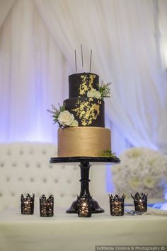 a black and gold wedding cake sitting on top of a table next to small candles