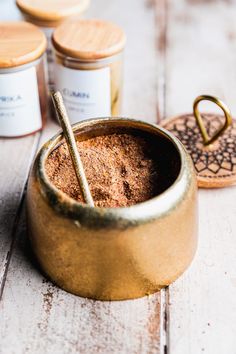 some spices are in a small bowl on a table next to other spice jars and spoons