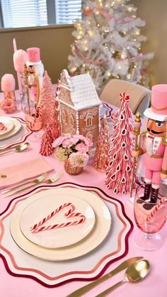 a table set for christmas with pink and gold decorations, candy canes, gingerbread houses, and trees