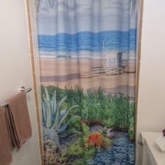 a bathroom with a shower curtain that has a beach scene on it and flowers in the water