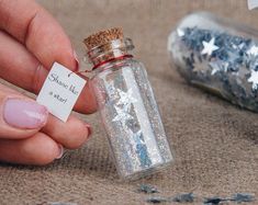 a hand holding a tiny bottle filled with glitter next to a house and confetti