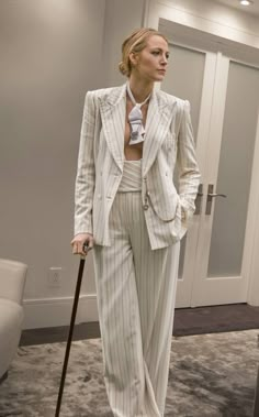 a woman in a white suit and hat with a cane standing on the floor next to a door