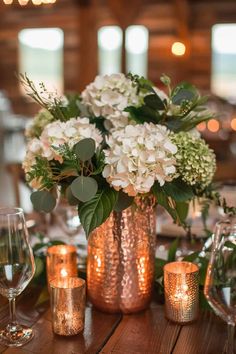 a vase filled with white flowers sitting on top of a wooden table next to candles