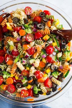 a bowl full of pasta salad with olives, tomatoes, broccoli and other vegetables