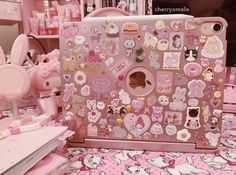 a pink laptop covered in lots of stickers on top of a table next to other items