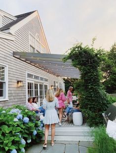 a group of people sitting on top of a wooden deck next to a house with blue hydrangeas