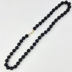 This onyx bead necklace features 8mm black onyx beads measuring 16 inches in length and with a 14 Karat yellow gold clasp. Black Onyx Necklace With Gemstone Beads, Black Gemstone Round Beads Jewelry, Black Gemstone Beads Jewelry, Black Onyx Round Bead Necklace, Black Onyx Gemstone Beads, Classic Pearl Necklace With Gemstone Beads, Classic Round Pearl Necklace With Gemstone Beads, Classic Single Strand Onyx Necklace, Classic Onyx Single Strand Necklace