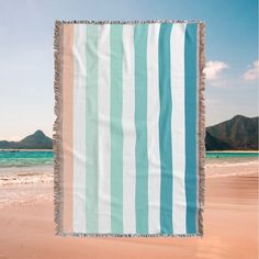 a blue and white striped beach towel hanging from the side of a sandy beach with mountains in the background