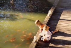 a woman sitting on a dock next to a pond filled with goldfish and looking at the water