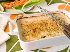 a casserole dish with cheese and vegetables on the table next to utensils