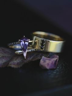 A dark & moody wedding ring set from Staghead Designs sits on a purple fall leaf. This ring set has a custom-made 14K yellow gold snake ring that has black diamond accents & our "Lilac" Mine Stone as the center stone - a 1.68ct shield cut purple spinel. Also seen is the "Orion" design 14K yellow gold wedding band with three vertical black diamond accents. These rings can also be made in 14K rose or white gold & with a variety of unique gemstones. Find or design your dream rings today! Whiskey Barrel Wedding Ring, Spinel Engagement Ring, Black Diamond Wedding Band, Antler Wedding Rings, Matching Wedding Ring Sets, Orion Black, Spinel Engagement Rings, Snake Black, Black Diamond Wedding Bands