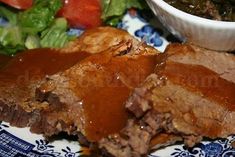 a blue and white plate topped with meat next to a bowl of sauce on top of a salad