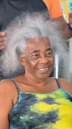 an older woman with white hair and greying is smiling at the camera while another person stands behind her