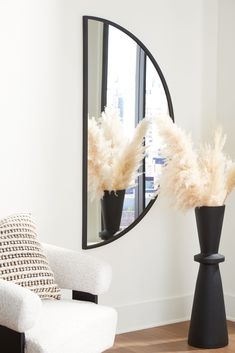 two black vases with white feathers in front of a large mirror on the wall