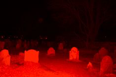 a cemetery at night with red light from the ground and tombstones in the foreground