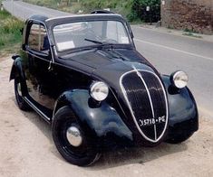 an old black car is parked on the side of the road