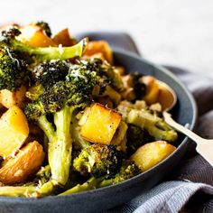 a bowl filled with broccoli and potatoes on top of a wooden table next to a blue towel