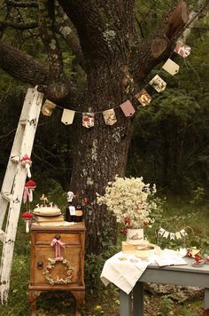 an old table with flowers and pictures on it next to a tree in the woods