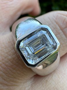 a close up of a person's hand holding a ring with an emerald stone