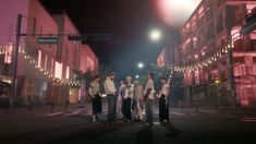 group of people standing in the middle of an empty street at night with lights on