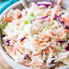 a bowl filled with coleslaw and carrots on top of a wooden table