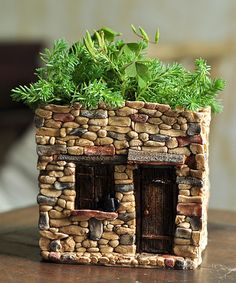 a small house made out of rocks with plants in the window sill on top