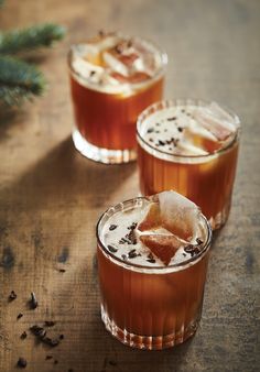 two glasses filled with drinks sitting on top of a wooden table next to a pine tree