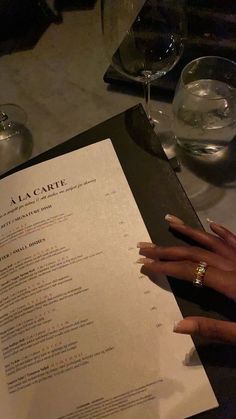 a woman's hand on top of a menu at a table with wine glasses