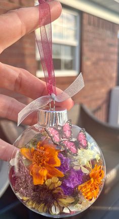 a hand holding a glass ornament filled with flowers