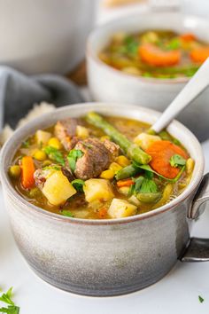 two bowls of soup with meat, vegetables and potatoes in them on a white surface