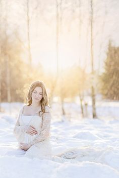 a pregnant woman sitting in the snow with her hands on her belly and looking at the camera