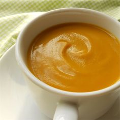 a white cup filled with orange liquid on top of a saucer next to a spoon